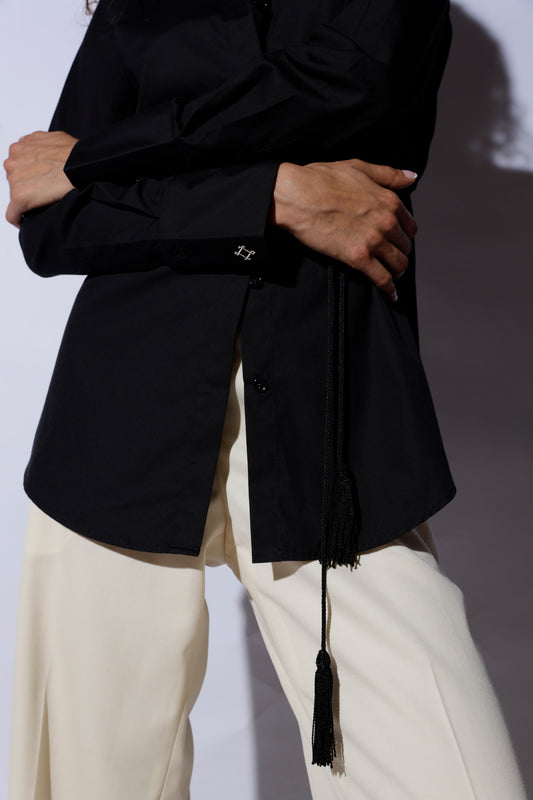 Person wearing a black shirt with a belt, standing against a plain background