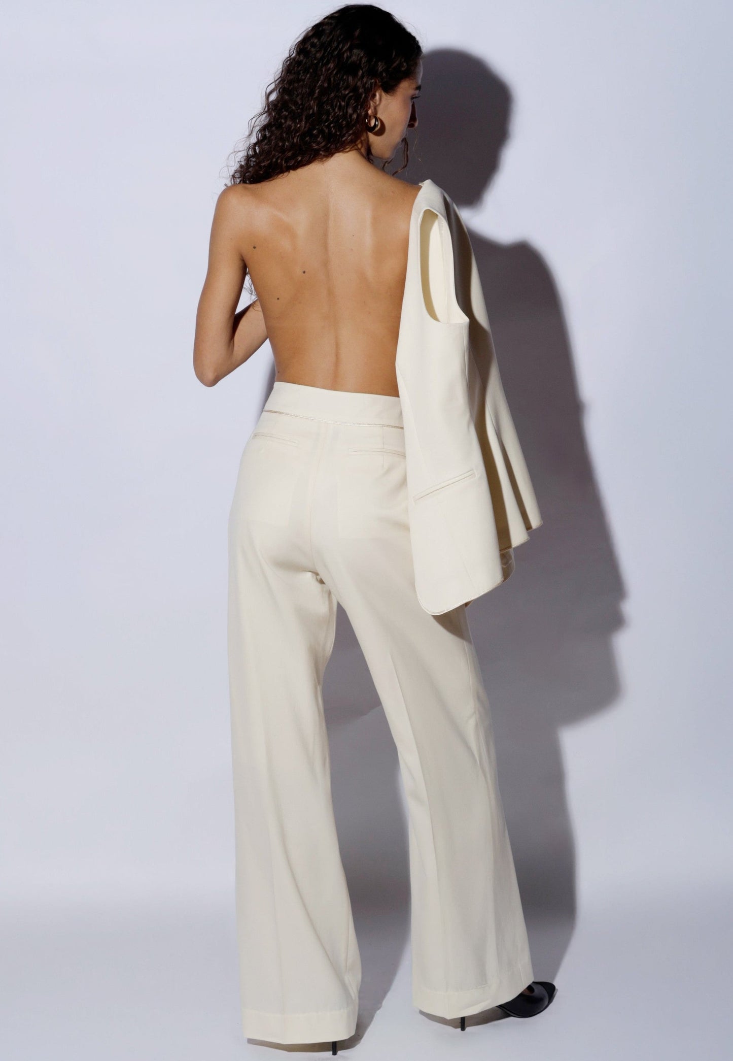 Woman wearing a white suit with a jacket over her shoulder against a plain background 100% wool 