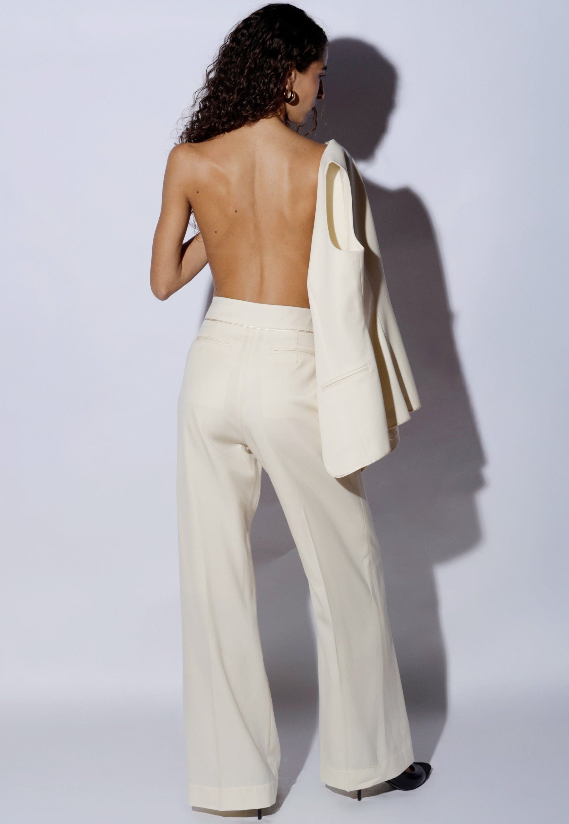 Woman wearing a white suit with a jacket over her shoulder against a plain background 100% wool 