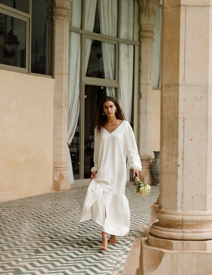 Woman in a white dress standing in an elegant interior setting with columns and patterned floor.