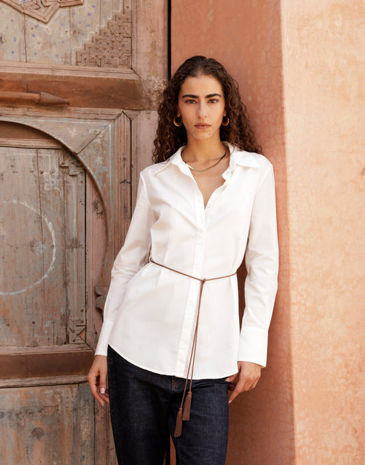 Woman in a white blouse standing against a textured wall.