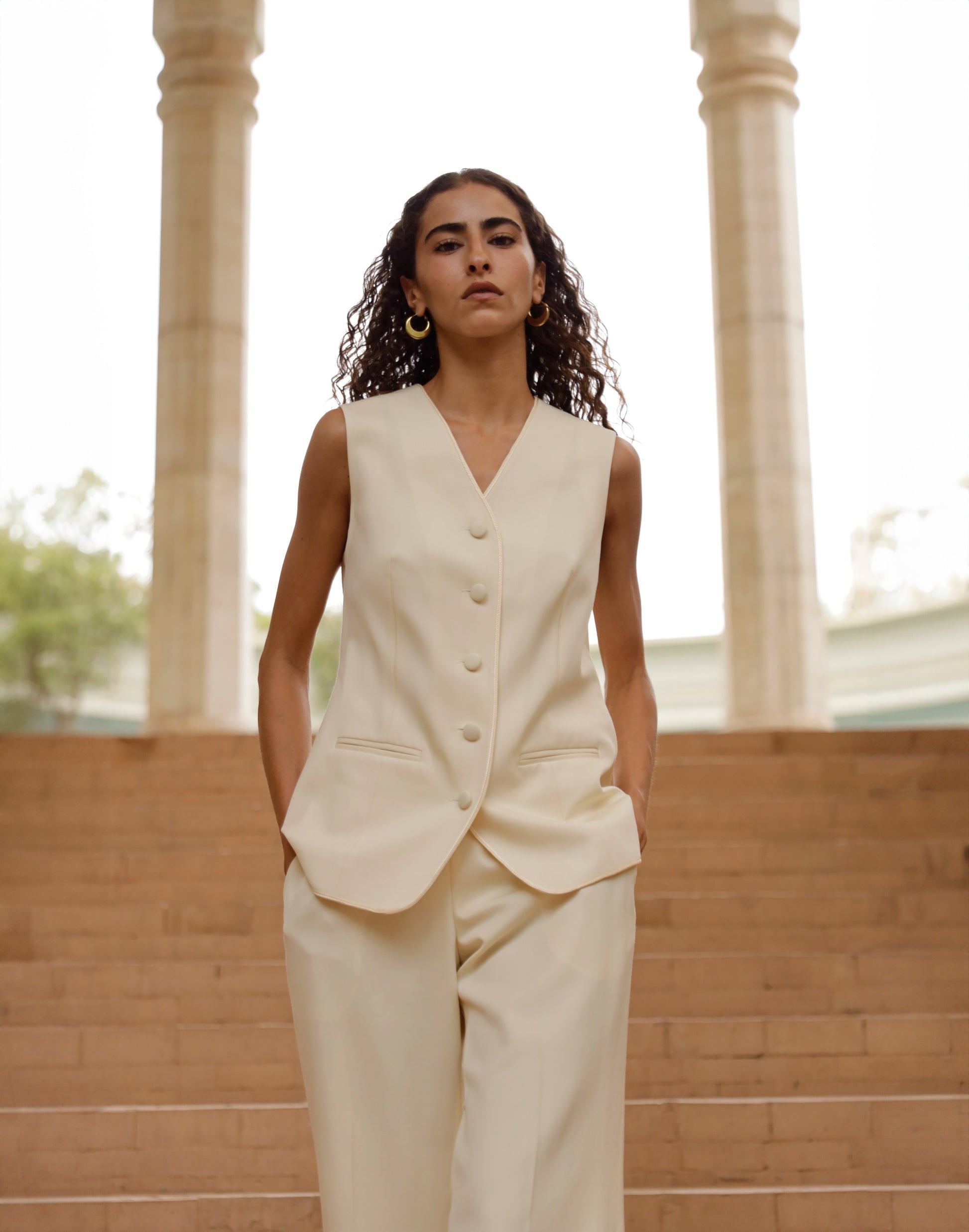 Woman wearing a cream-colored suit standing in front of columns.